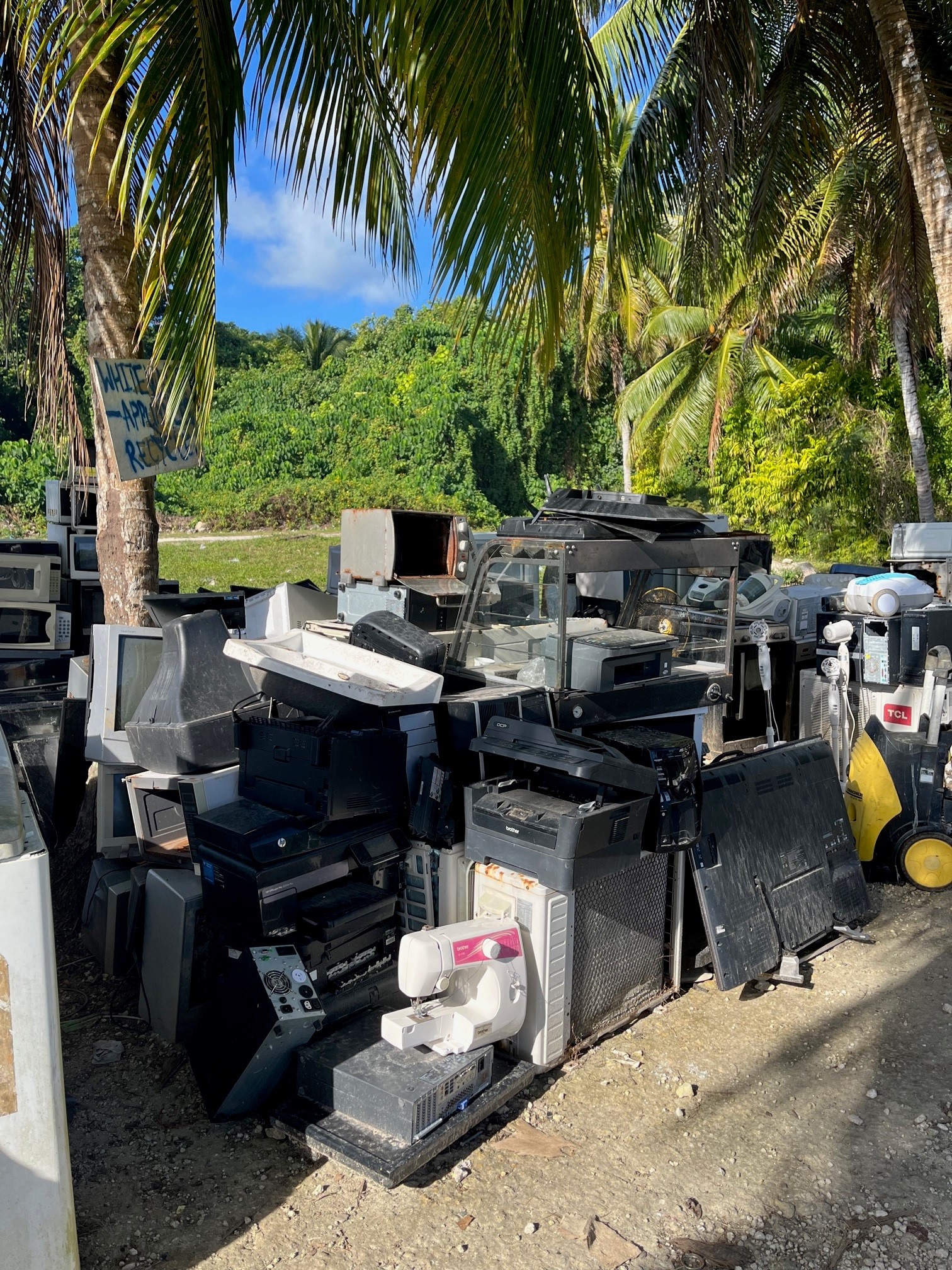 Large pile of discarded electronic waste under palm trees in the Pacific.